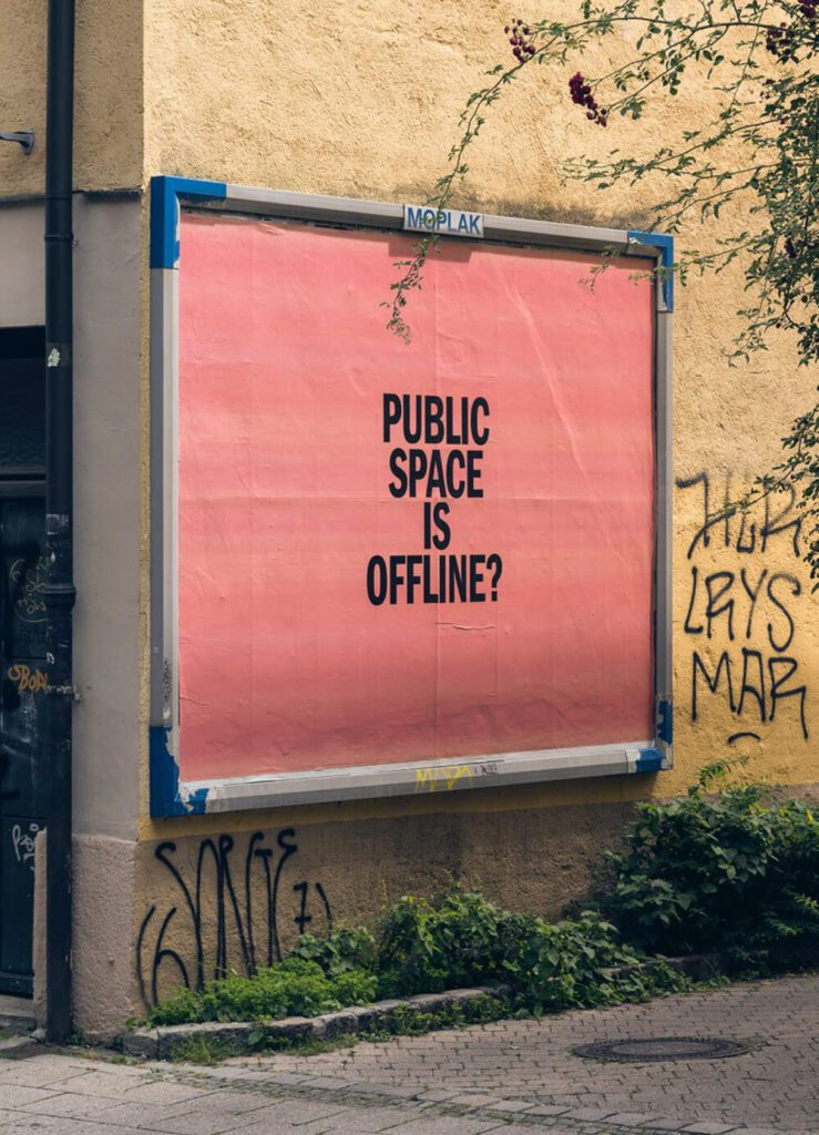 An einer gelben Hauswand mit einigen Graffiti hängt eine große Werbetafel. Sie zeigt ein großes rotes Plakat auf dem in schwarzen Großbuchstaben "PUBLIC SPACE IS OFFLINE?" zu lesen ist. Unterhalb des Plakats verläuft ein schmaler Grünstreifen.