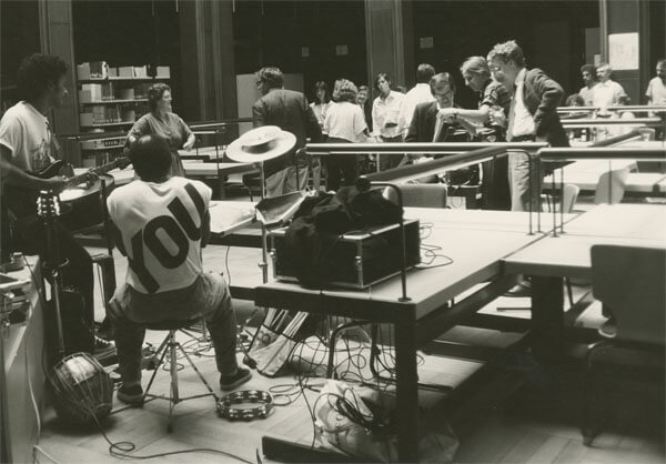 In einem großen Lesesaal mit vielen Schreibtischen tummeln sich einige Menschen. Im Vordergrund bauen gerade zwei Männer Technik und Instrumente auf.