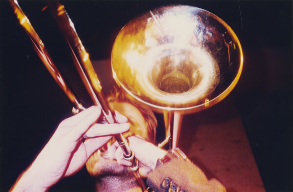 Das Bild zeigt eine goldene Posaune. Der dazugehörige Posaunenspieler wird durch sein Instrument beinah ganz verdeckt.
