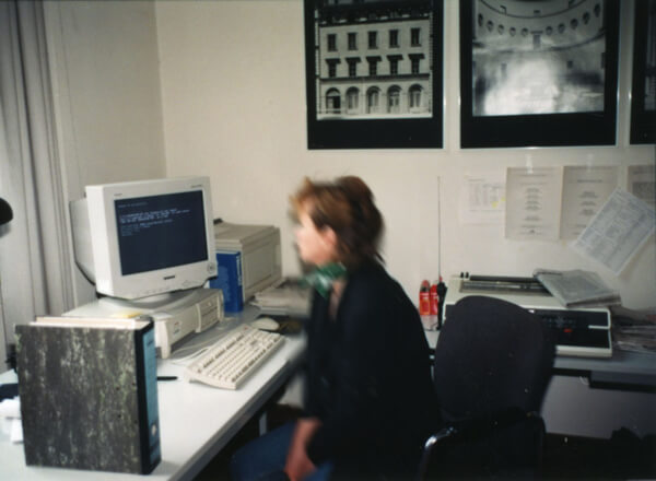 Frau am Schreibtisch in einem Büro. Auf dem Schreibtisch u.a. ein alter Personal Computer sowie eine elektronsiche Schreibmaschine. Foto von 1997