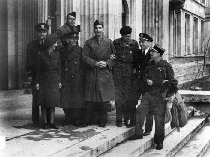 Schwarzweißfotografie von acht Personen in militärischen Uniformen auf den Treppen vor einem Haus.