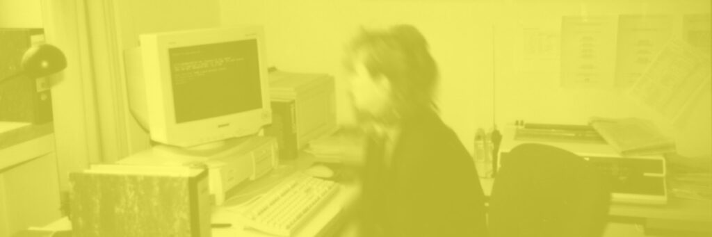 Eine Frau sitzt in einem Büro vor einem älteren Computer.