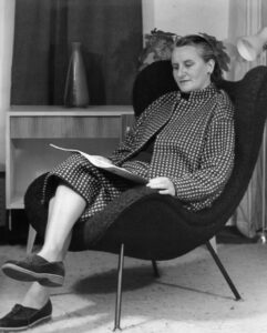 Eine Schwarzweißfotografie einer ältere Frau, die in einem Sessel sitzt und liest (Juliane Roh).