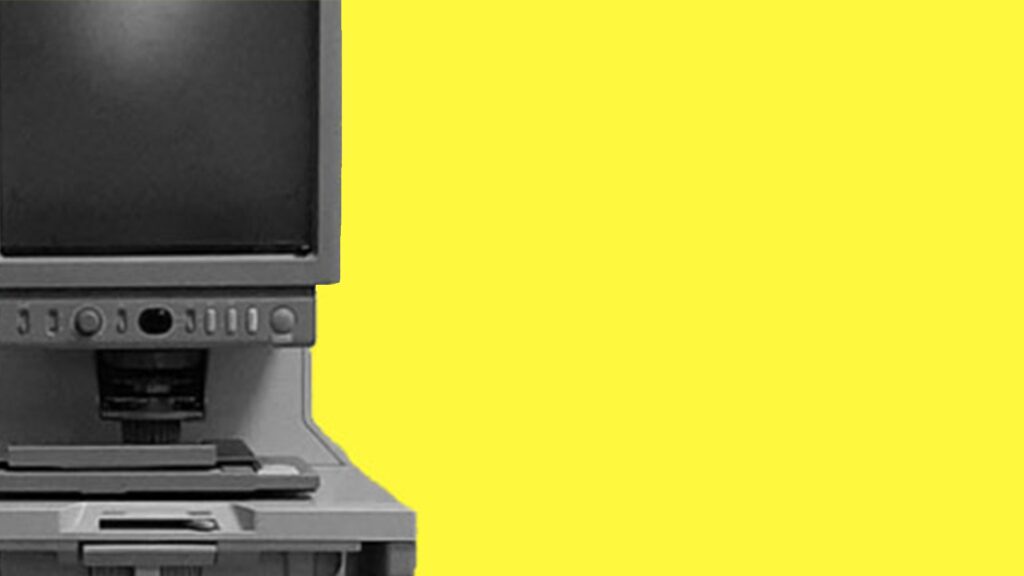Freigestellter Computer (Microfiche-Gerät) vor zitronengelbem Hintergrund.