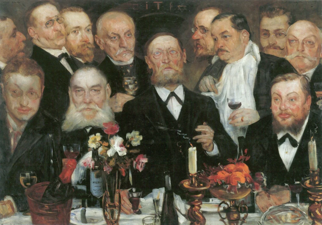 Mehrere Personen in formeller Kleidung sitzen an einem gedeckten Tisch mit Kerzen, Blumen, Weinflaschen und einem Hummergericht.