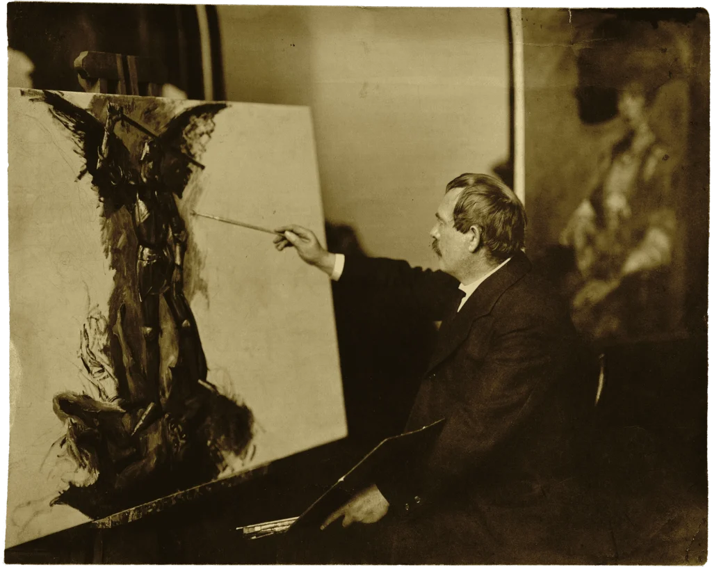 Mann im Anzug sitzt vor einer Staffelei und malt mit Pinsel auf einer großen Leinwand.