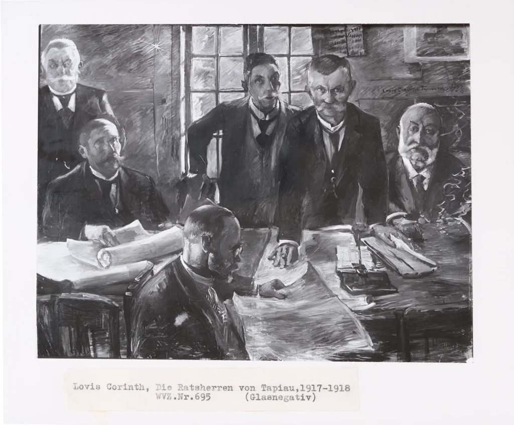 Fünf Männern in Anzügen in einem Raum mit großen Fenstern, einer sitzt an einem Tisch mit Papieren, die anderen stehen oder sitzen um ihn herum