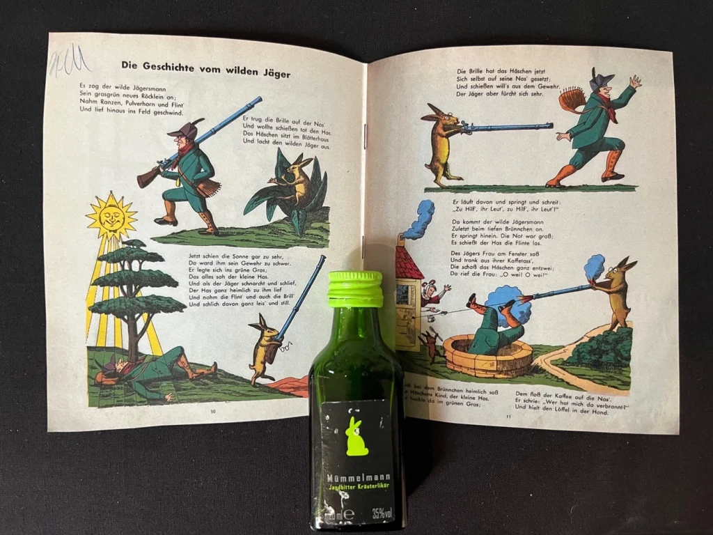 Aufgeschlagene Kinderbuchseite mit farbigen Illustrationen einer Geschichte vom wilden Jäger und einem kleinen grünen Fläschchen Mömmelmann Jagdbitter Kräuterlikör davor