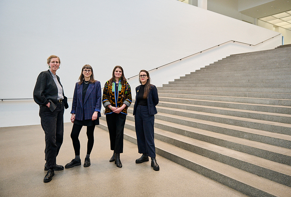 Vier Personen stehen vor einer breiten Treppe in einem modernen Innenraum mit weißen Wänden