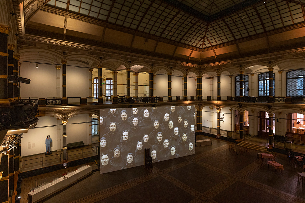 Großer historischer Saal mit Galerie und hängender Leinwand, die ein Schwarz-weiß-Foto mit mehreren Frauenporträts zeigt