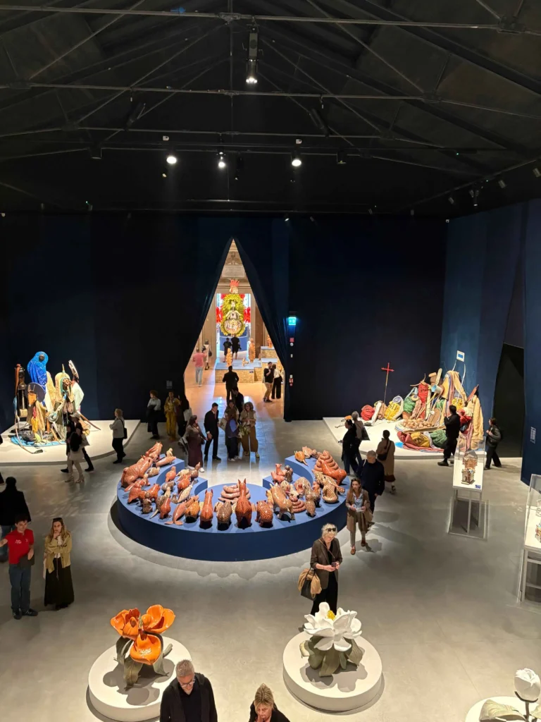 Großer Ausstellungsraum mit mehreren runden Podesten, auf denen bunte Skulpturen stehen, und Besuchern, die sich die Exponate ansehen